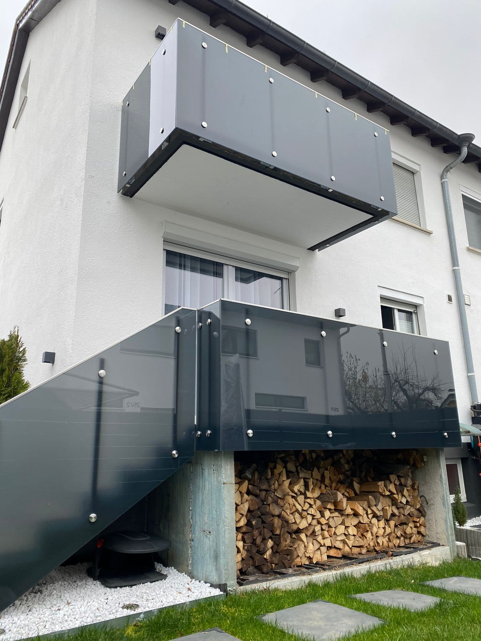 Auskragender Balkon und darunterliegende Terrasse mit dunklem Glasgeländer und seitlicher Treppe